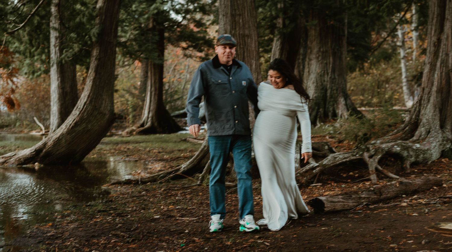 A couple explores a forest path together during an autumn photoshoot.