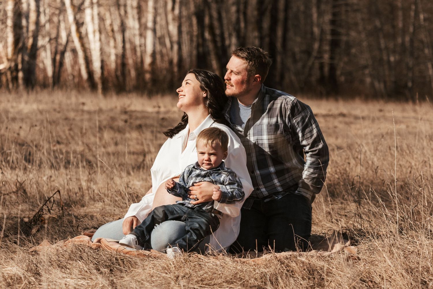Family sits together in golden field during autumn photo session.