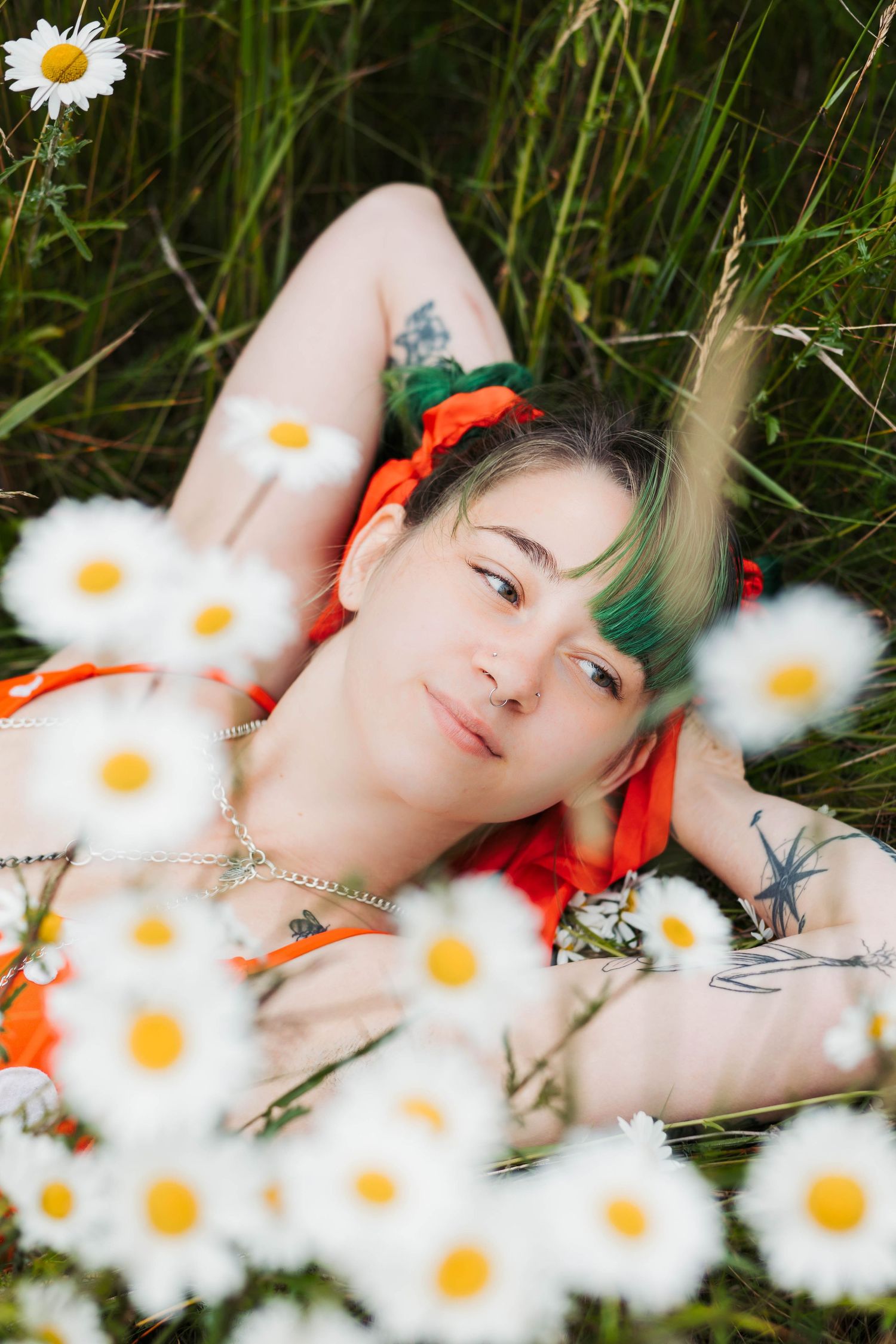 Dreamy outdoor portrait surrounded by blooming daisies featuring green hair and orange accessories.
