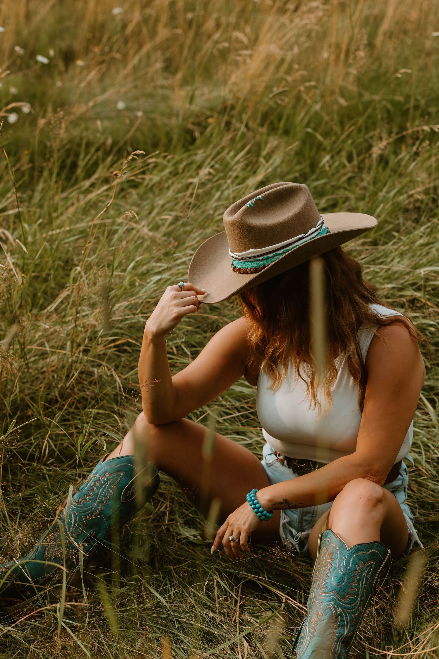 Western style portrait with turquoise boots and brown cowboy hat in tall grass.