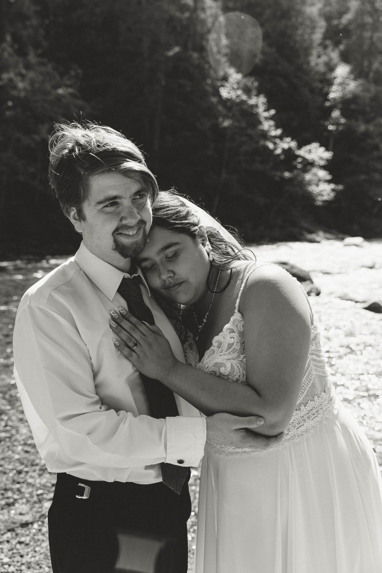 Black and white portrait of couple sharing tender moment by riverbank.