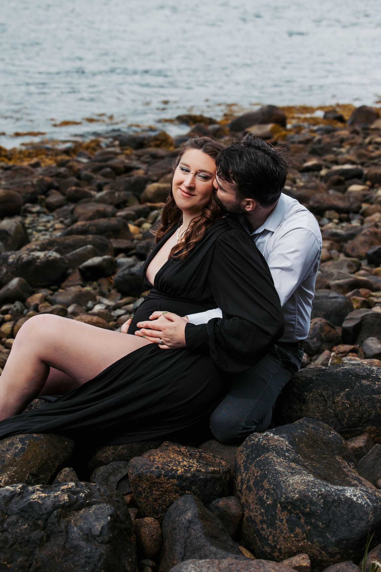 A tender embrace shared on rocky coastline with ocean and mountains behind.