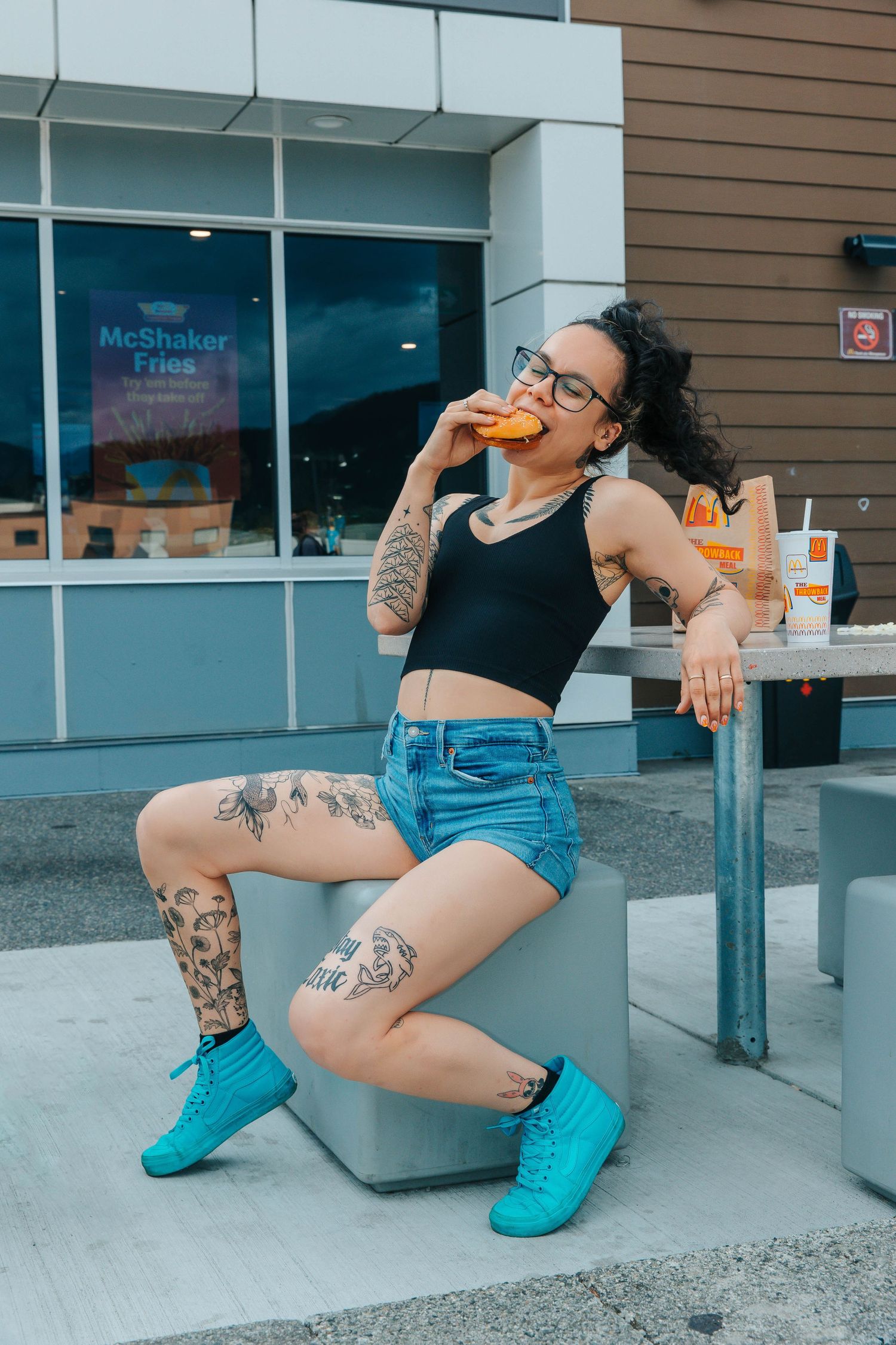 Playful fast food portrait with tattoos and bright footwear enjoying a burger.