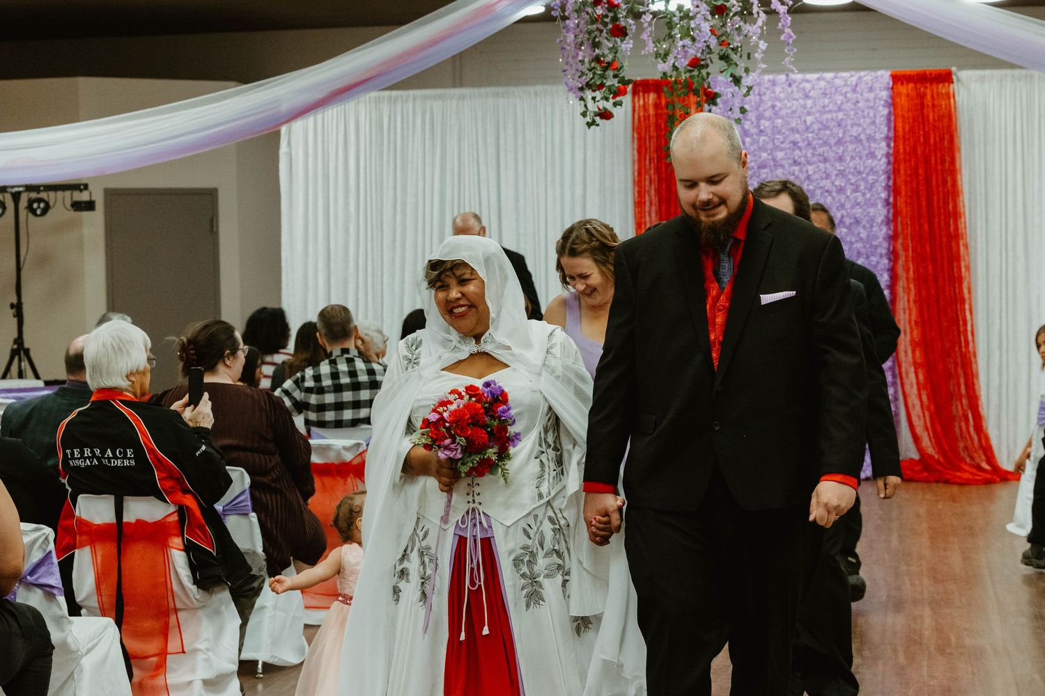 Wedding couple walking down aisle after ceremony with red and white decorative backdrop.