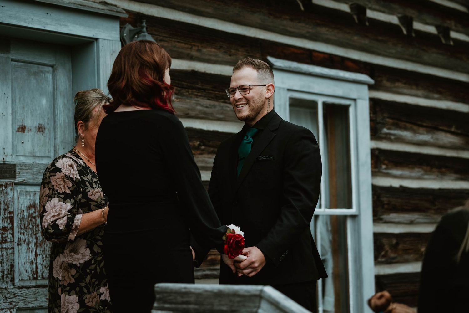 Ceremony taking place outside rustic log cabin with white flower.