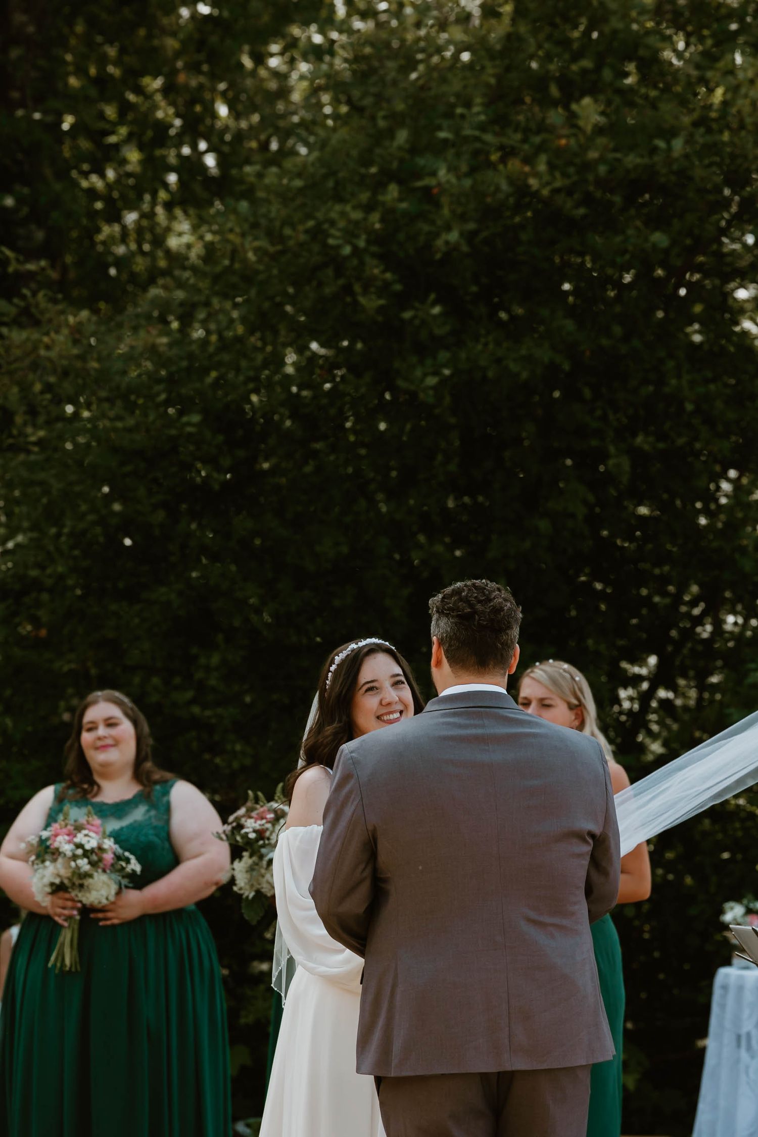 An outdoor wedding ceremony features bridesmaids in green dresses and a couple at the altar.
