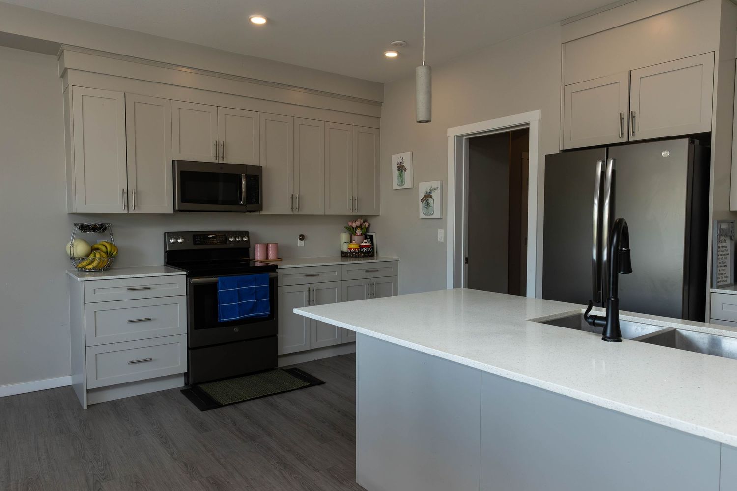 Modern white kitchen with black appliances, quartz countertops, and hardwood floors features a spacious central island.