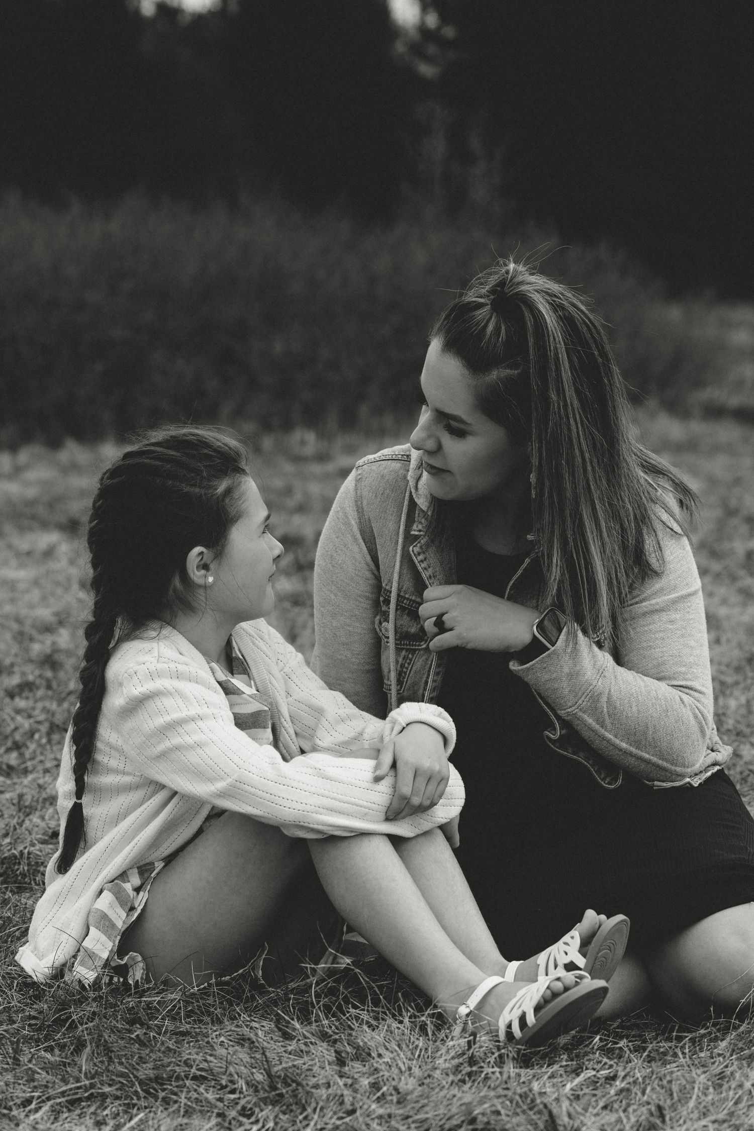 Intimate black and white portrait of parent and child sitting together in grass.