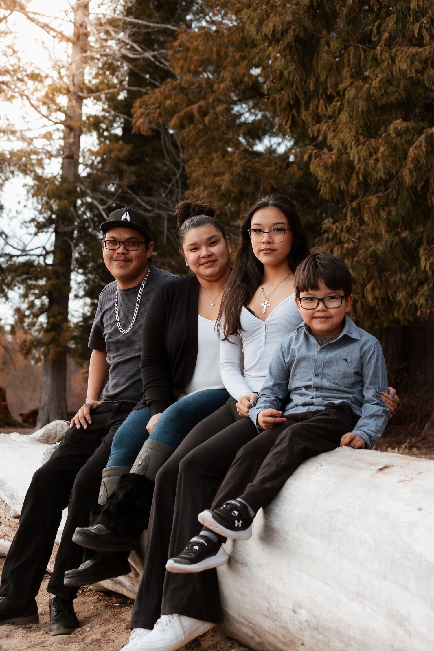 Family sitting together on white ledge against evergreen trees at sunset.