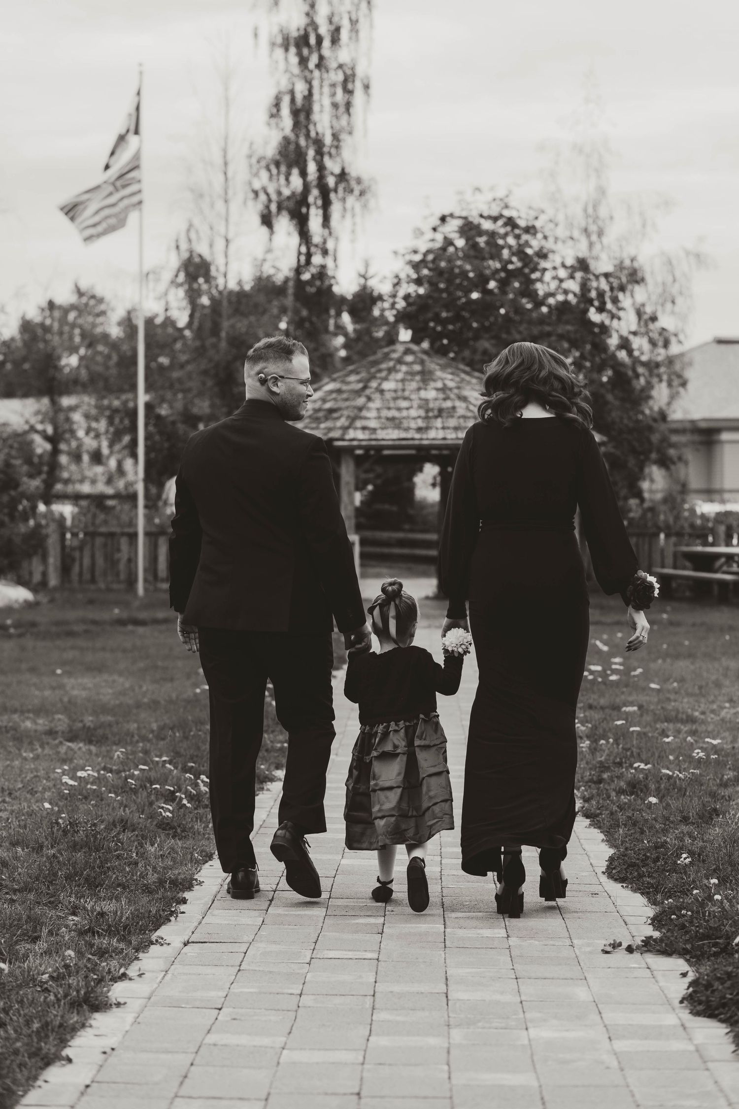 Black and white photo of three people walking down a path with American flag in background.
