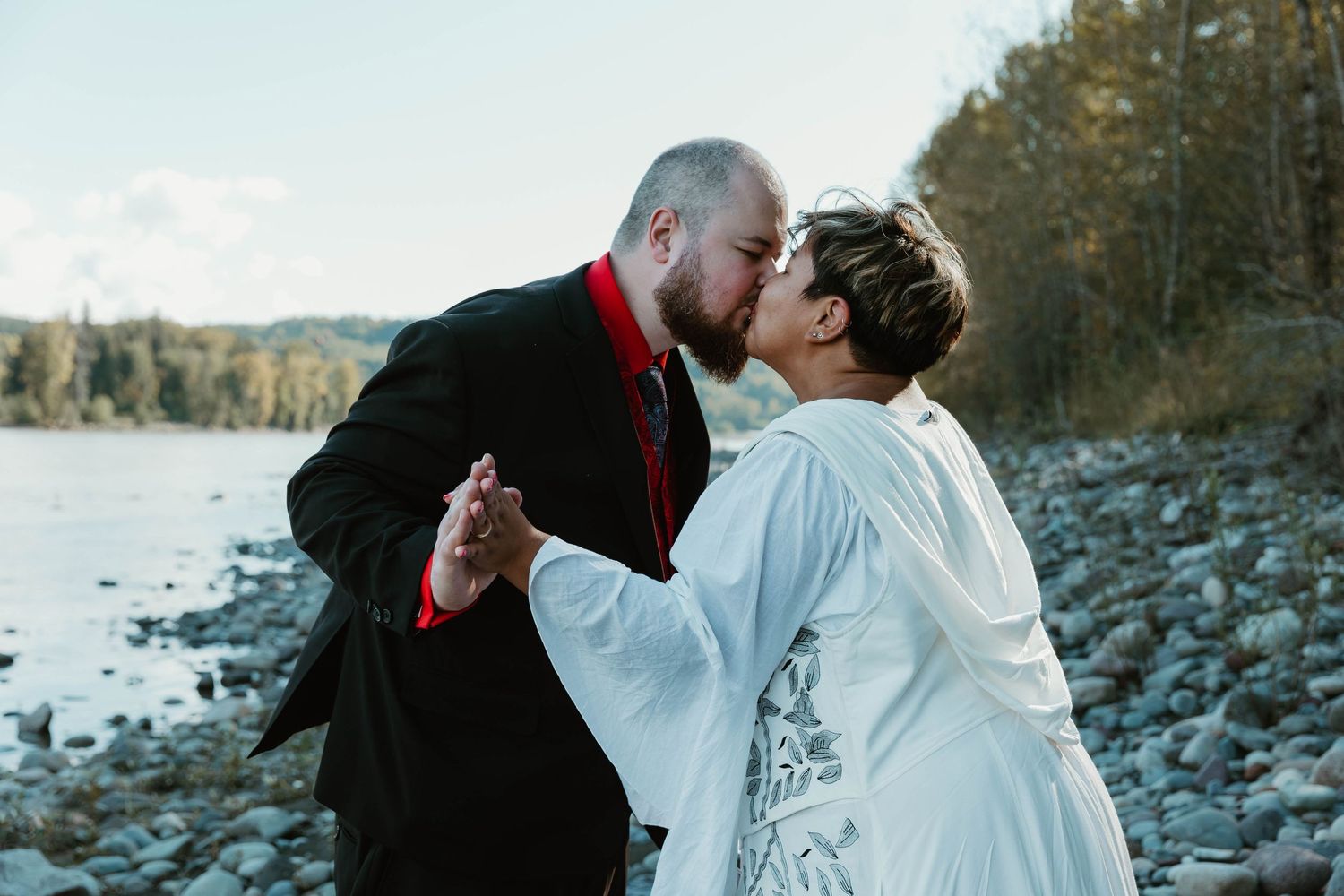 Dancing couple shares romantic moment by river with mountains in background.