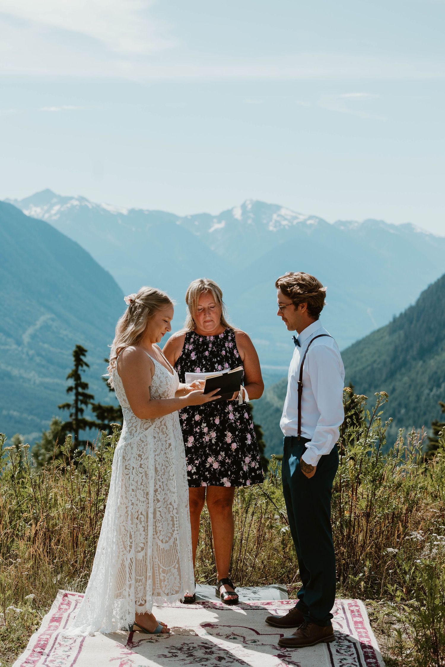 A small wedding ceremony unfolds on a decorative rug with majestic mountain peaks in the distance.