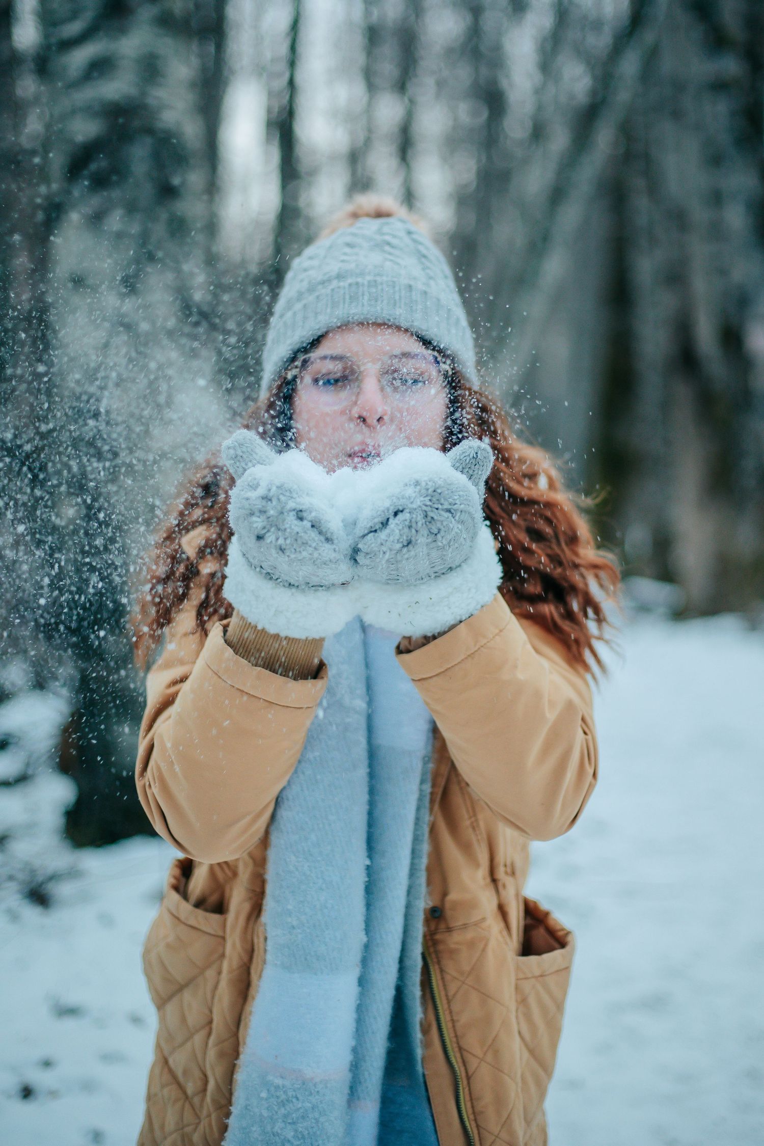 Winter portrait blowing snow from mittened hands wearing knit hat and scarf.