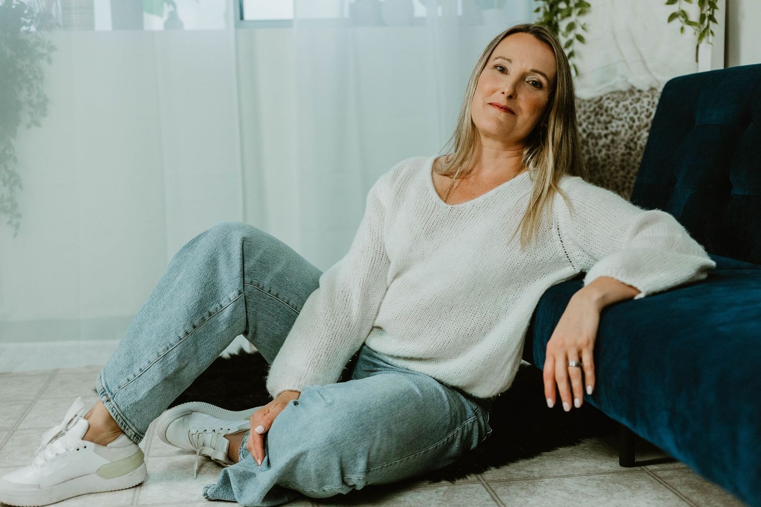 Relaxed lifestyle photo lounging on navy couch wearing white sweater and jeans.