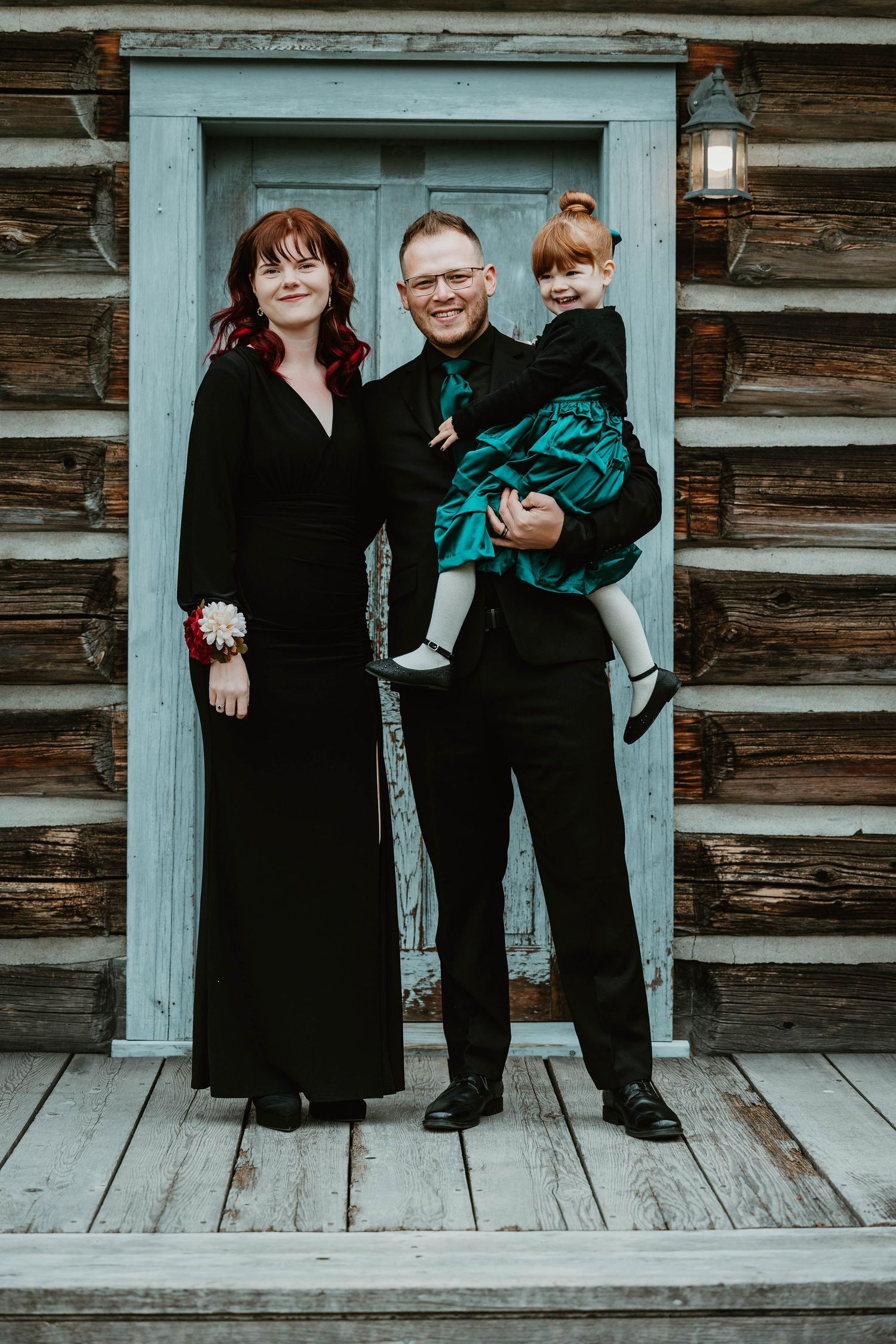 A family poses together on a rustic cabin porch with white door and wooden walls.
