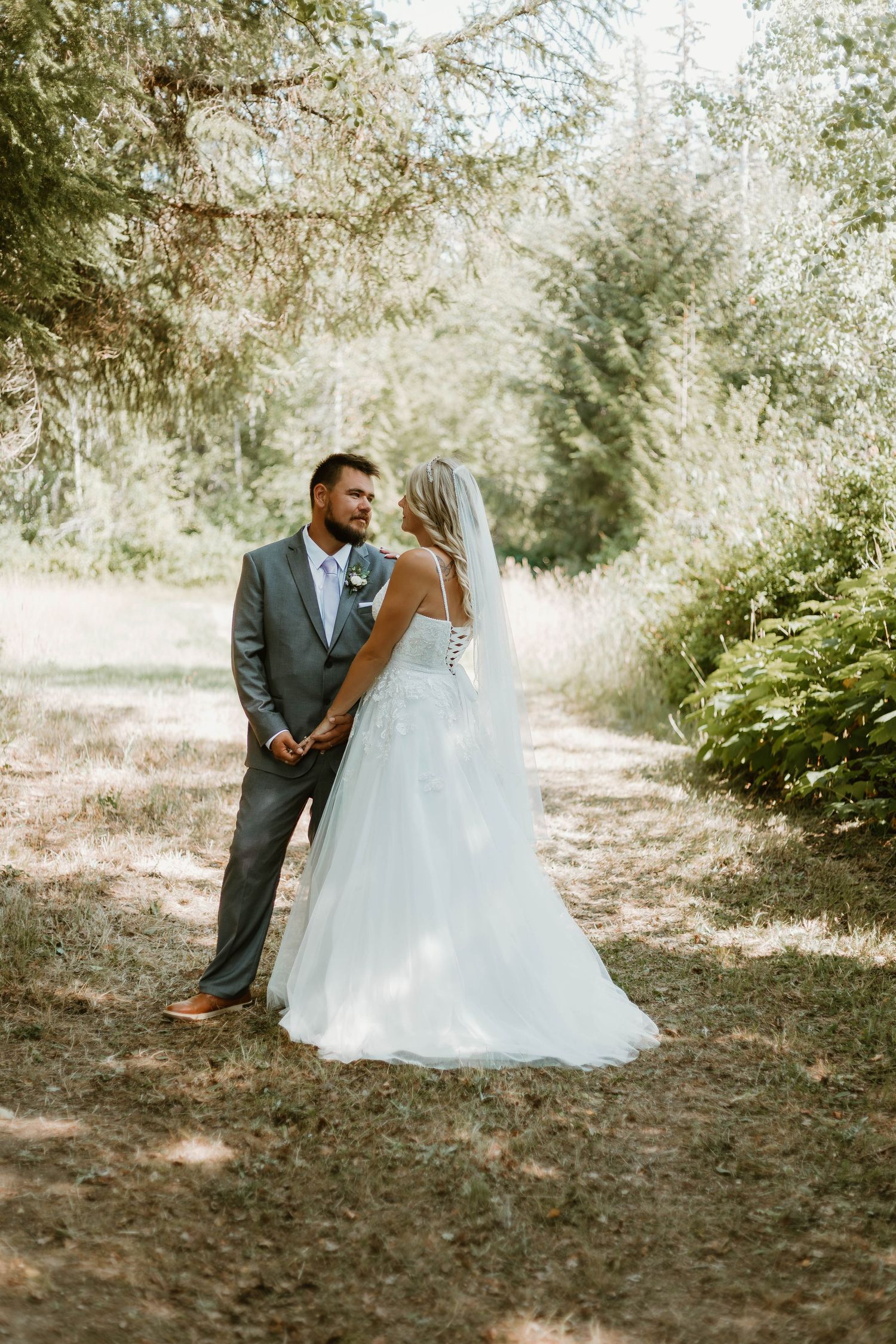 A newlywed couple poses together on a sunlit forest path during their wedding photoshoot.