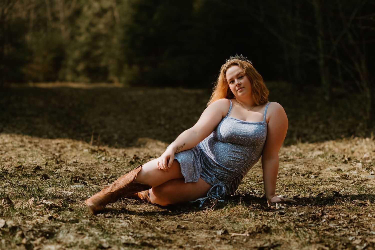 Someone in a light blue dress poses on the ground during a sunlit outdoor photo session in nature.