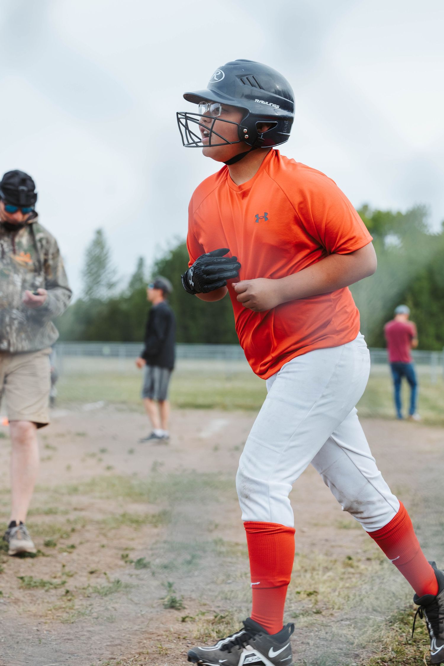 Baseball player in orange jersey and white pants running on a dirt field during a game.