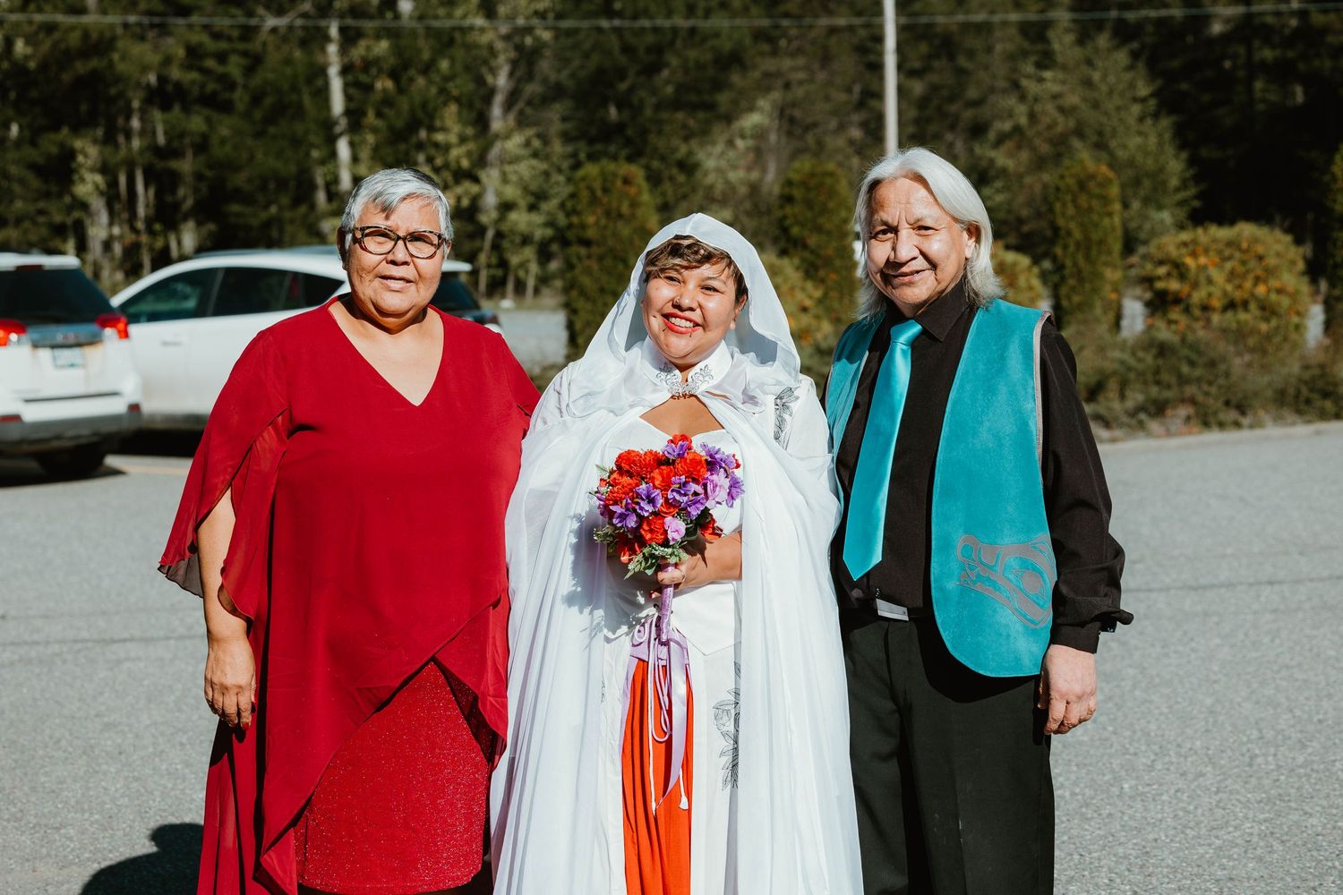 Wedding group poses outdoors with bright colorful attire and floral bouquet.