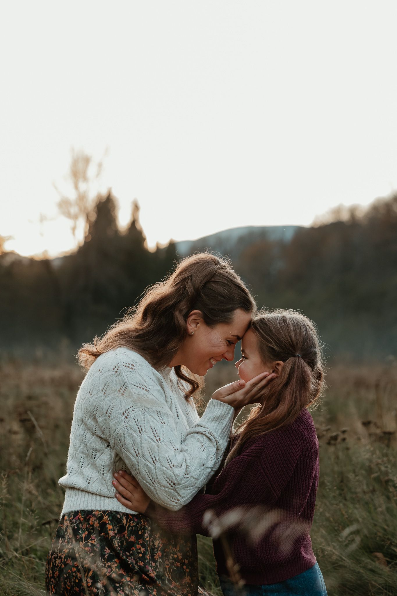 Two people in warm sweaters share an intimate moment together in a golden field at sunset.