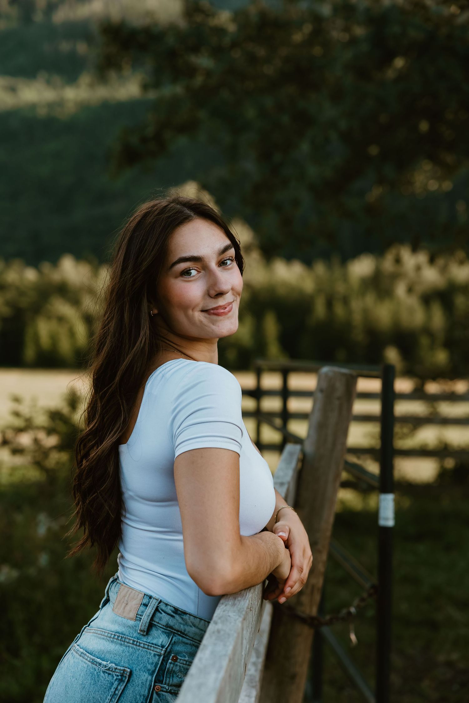 A person in a white t-shirt and blue jeans poses playfully against a rustic wooden fence at sunset.