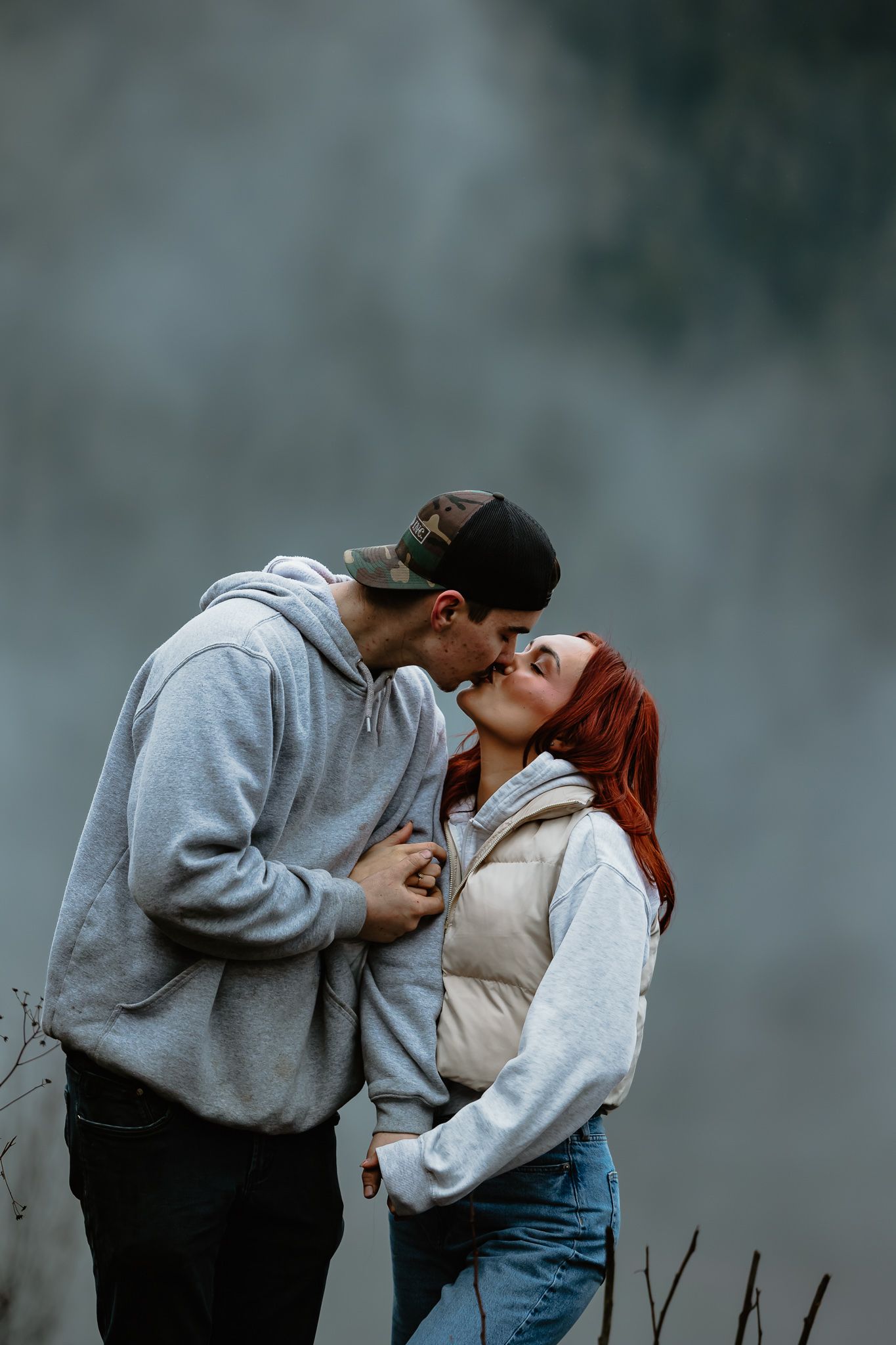 A couple in casual winter wear sharing a romantic kiss outdoors on a misty day.
