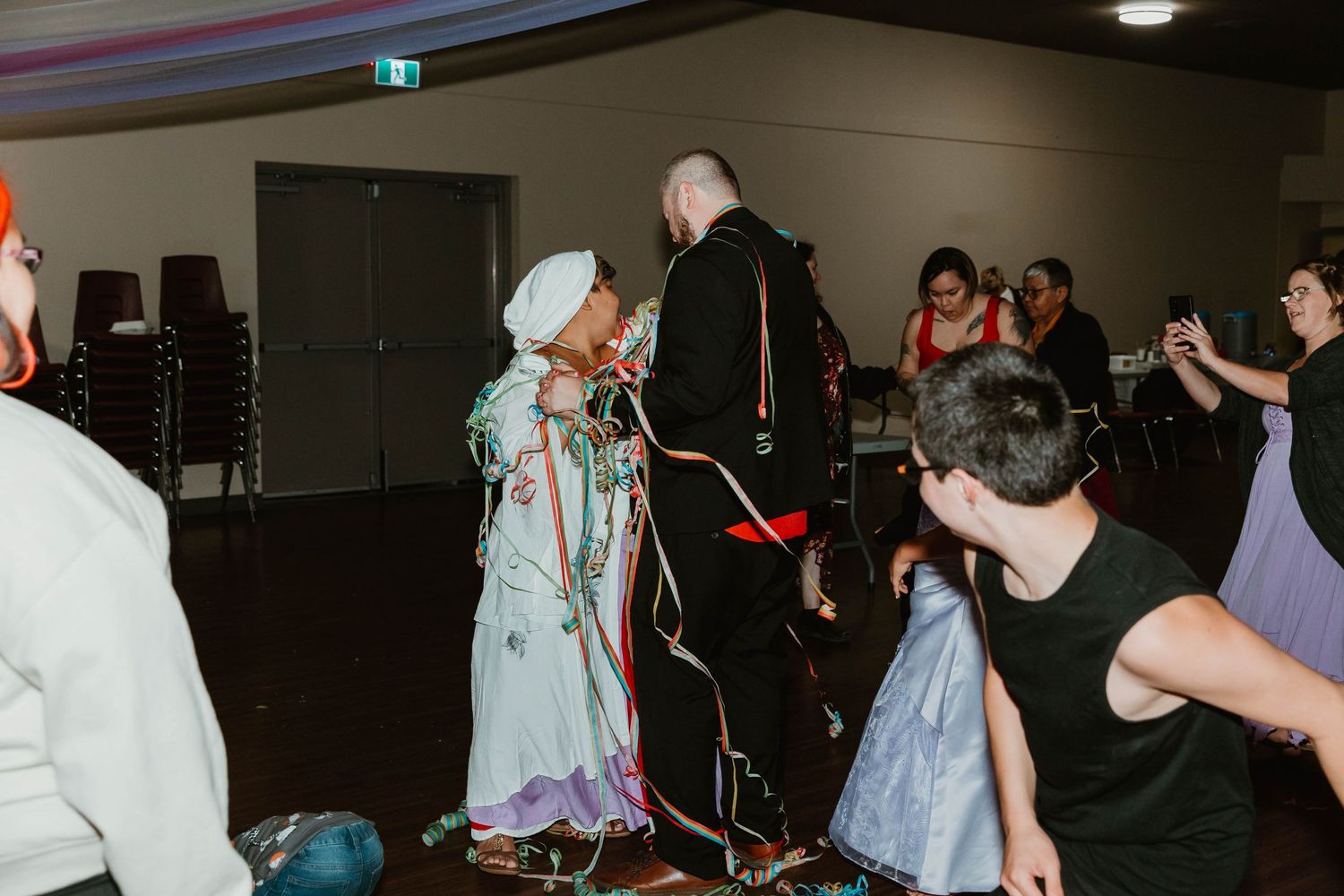 People dancing and celebrating at an indoor event with decorative lighting.