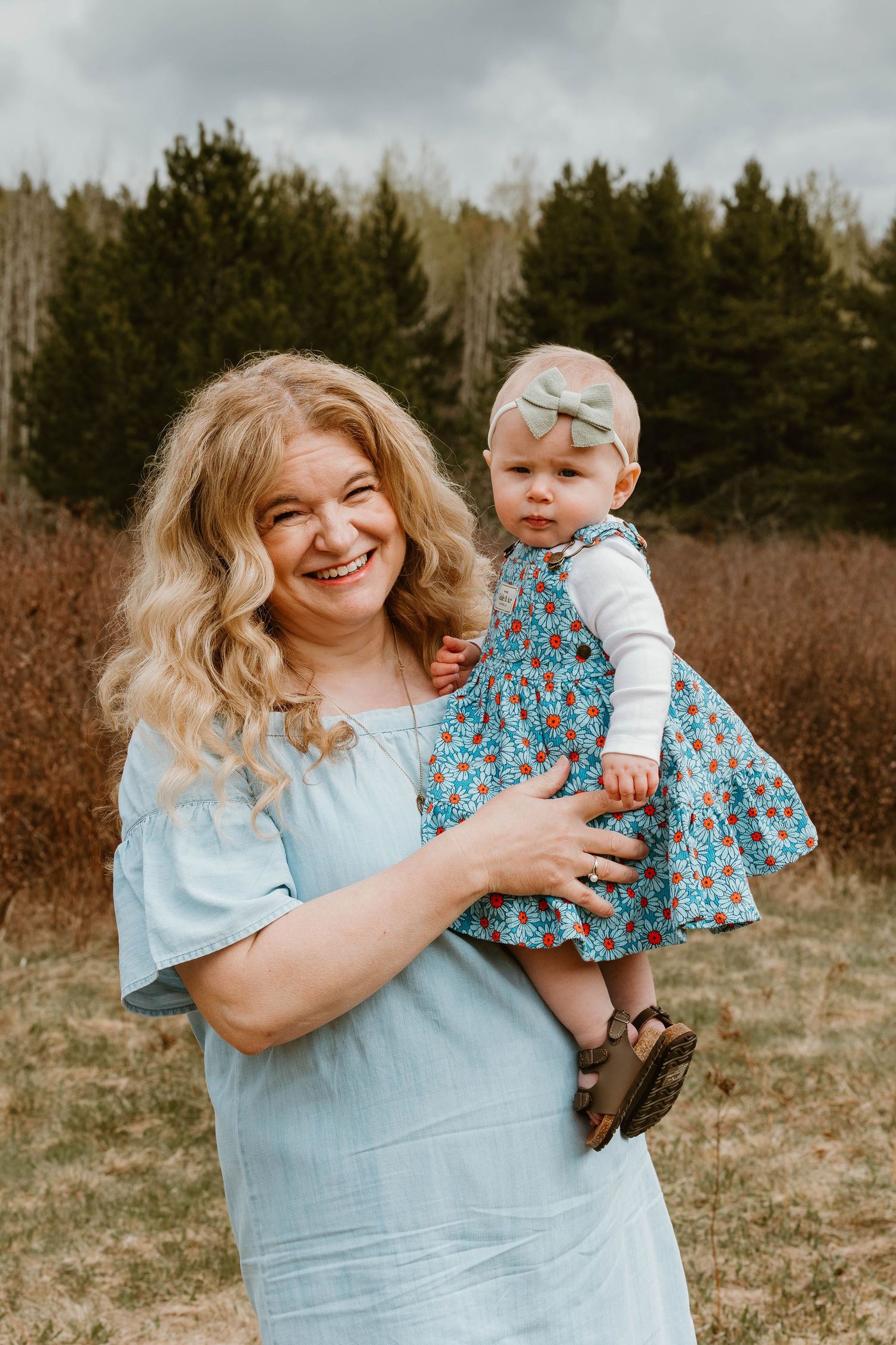 A tender moment shared outdoors with a baby wearing a floral dress and bow.