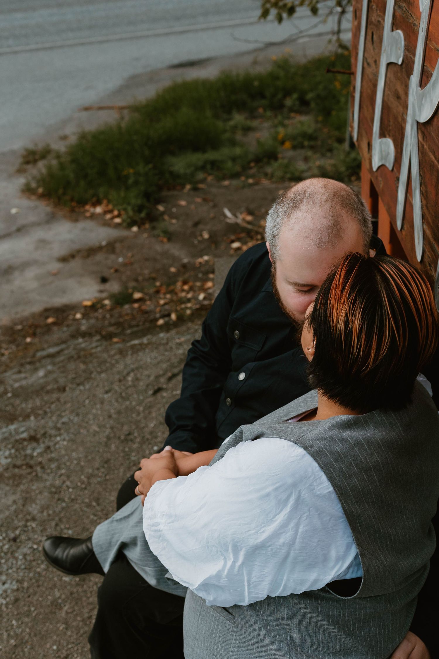 An intimate couple sitting close together outdoors in casual attire.
