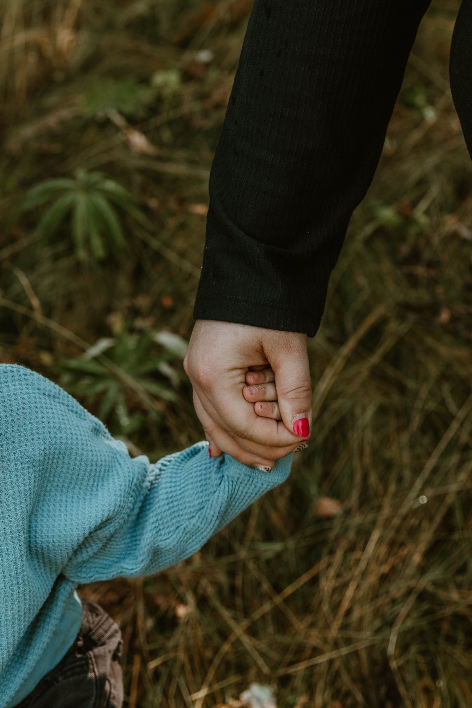 Close-up of hands holding each other against grassy outdoor background.