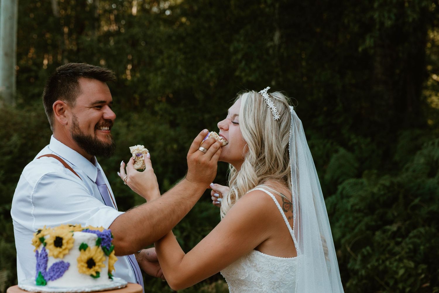 Couple playfully feeding each other cake at their outdoor wedding reception.