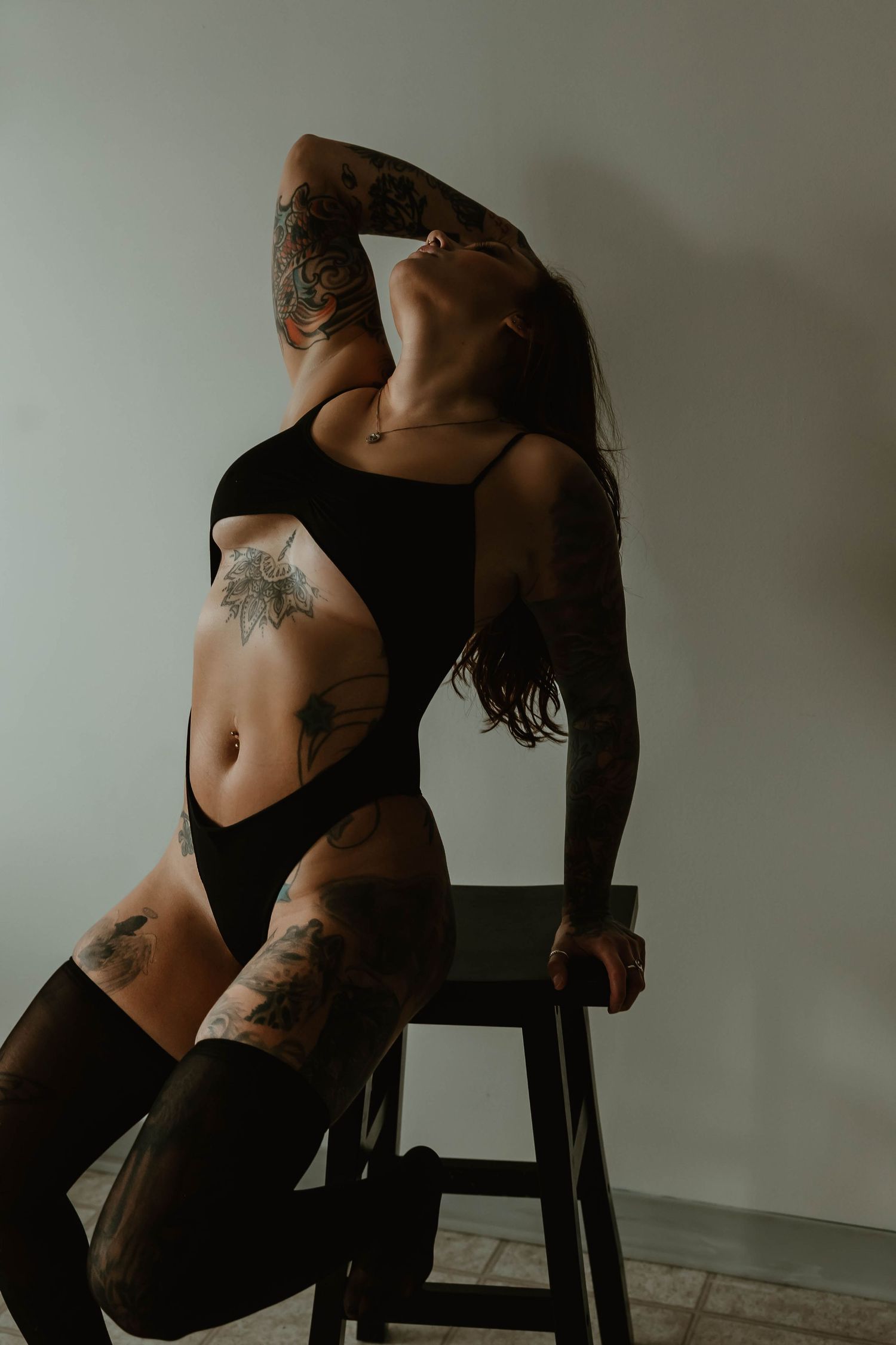 Artistic portrait showcasing tattoo art on person posing with black outfit on stool.