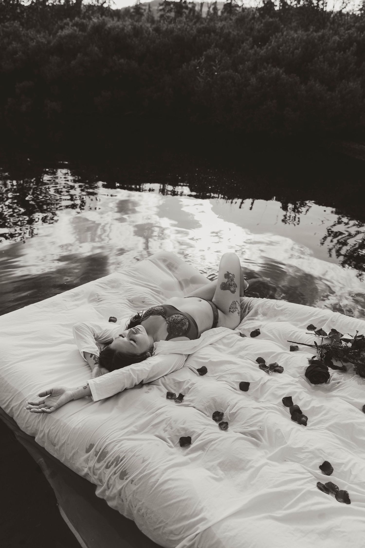 Black and white photo of person lounging on floating platform with rose petals.