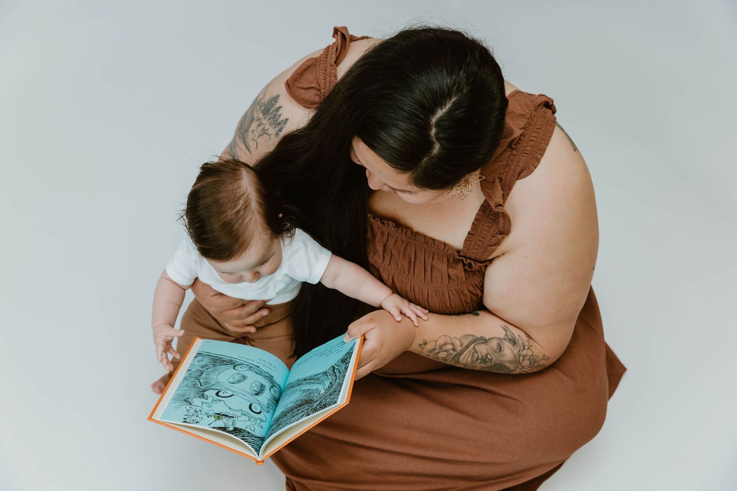 A parent and child share a tender moment while reading a book together, viewed from above against white background.