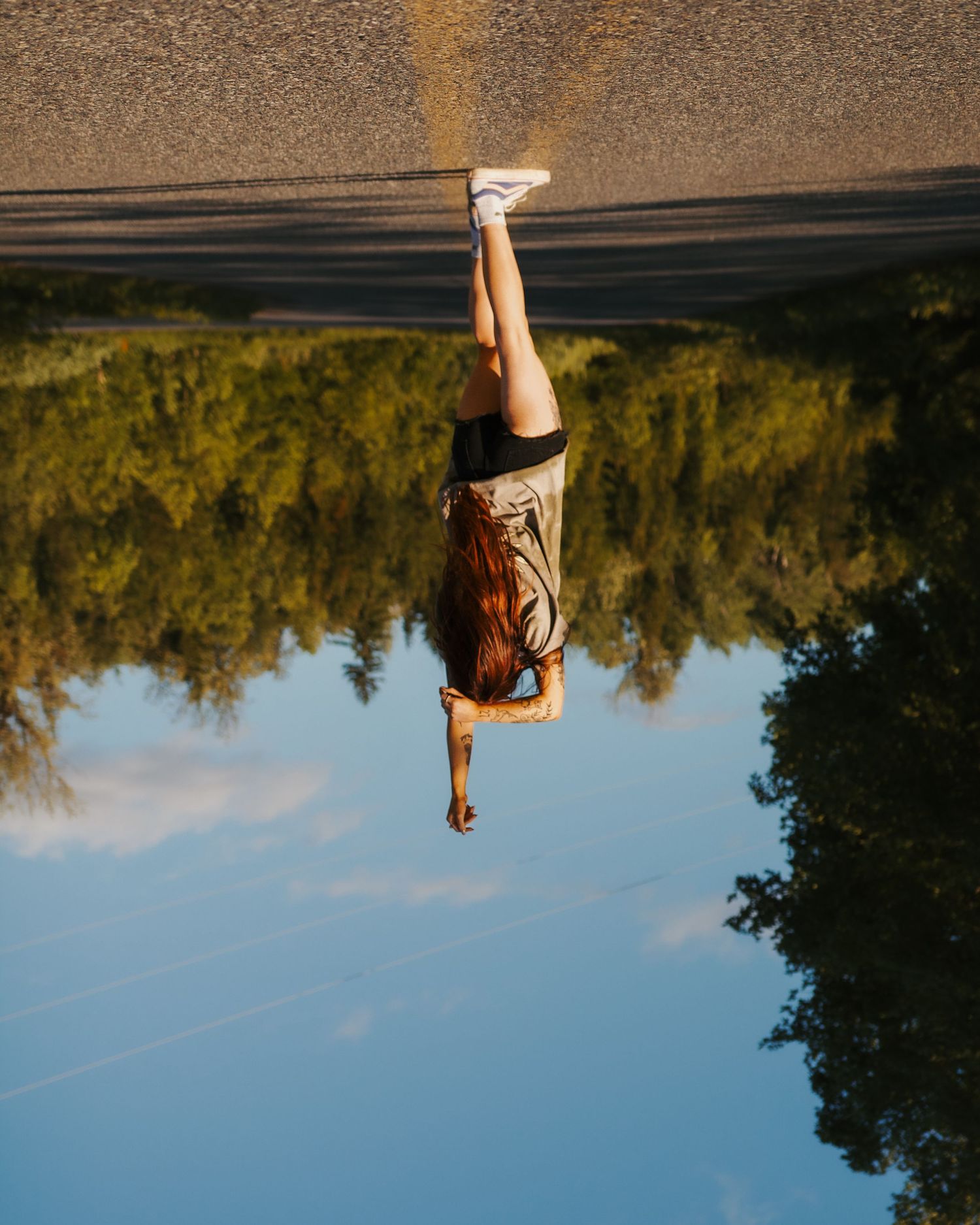 Creative upside down portrait reflection in still water with trees and sky in background.