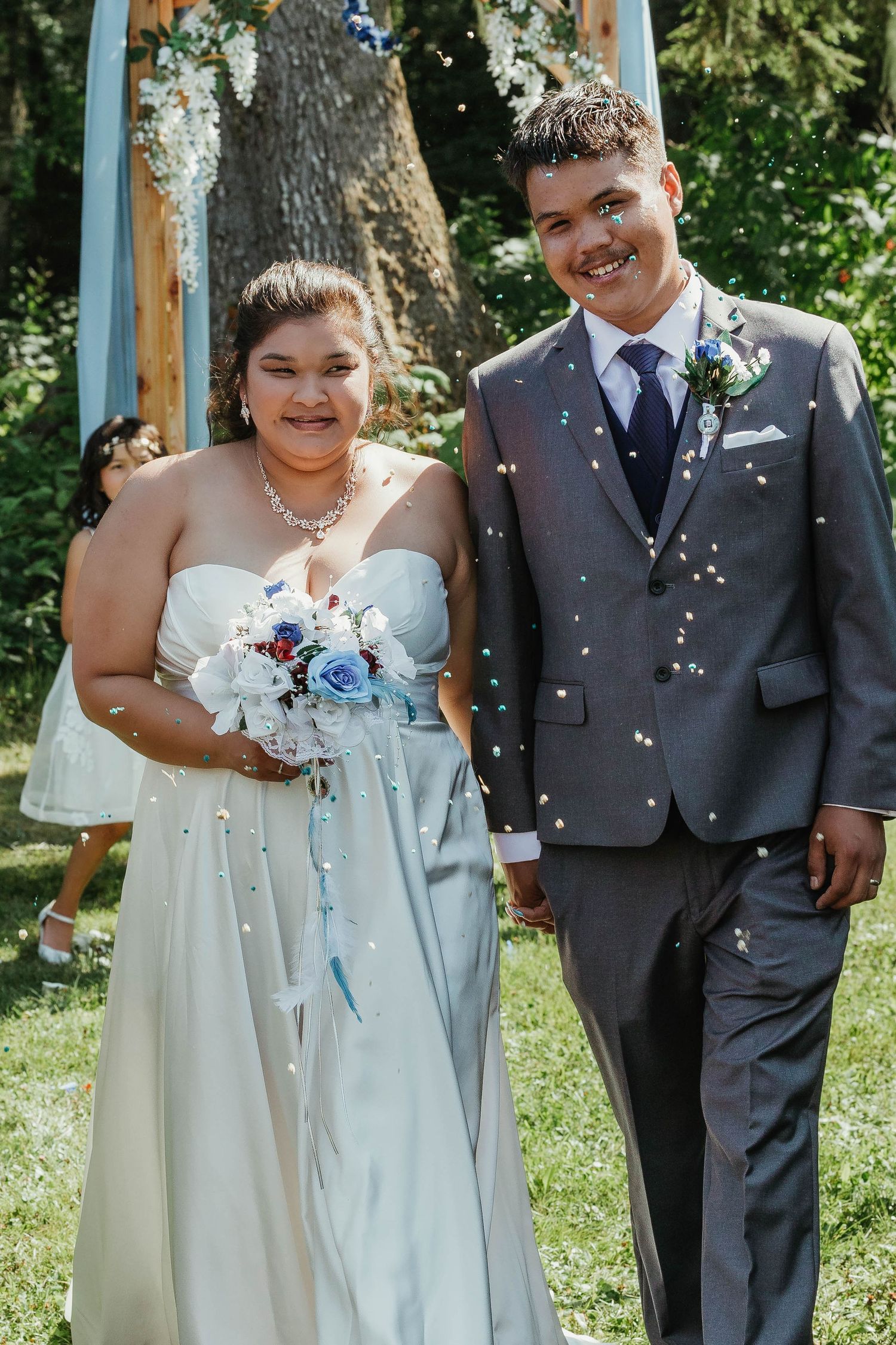 A happy couple shares a joyful moment under their wedding arch with confetti falling around them.