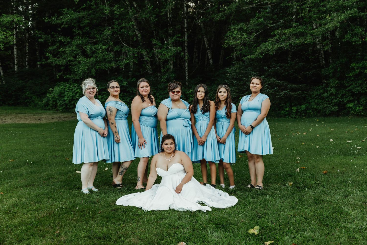 Wedding party poses on grass with bridesmaids in light blue dresses.