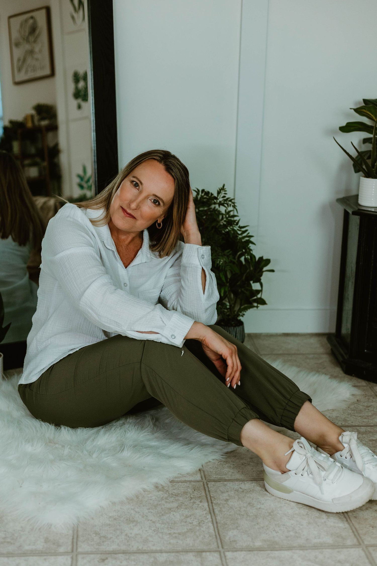 Casual indoor portrait sitting on white rug wearing white button-down and olive pants.