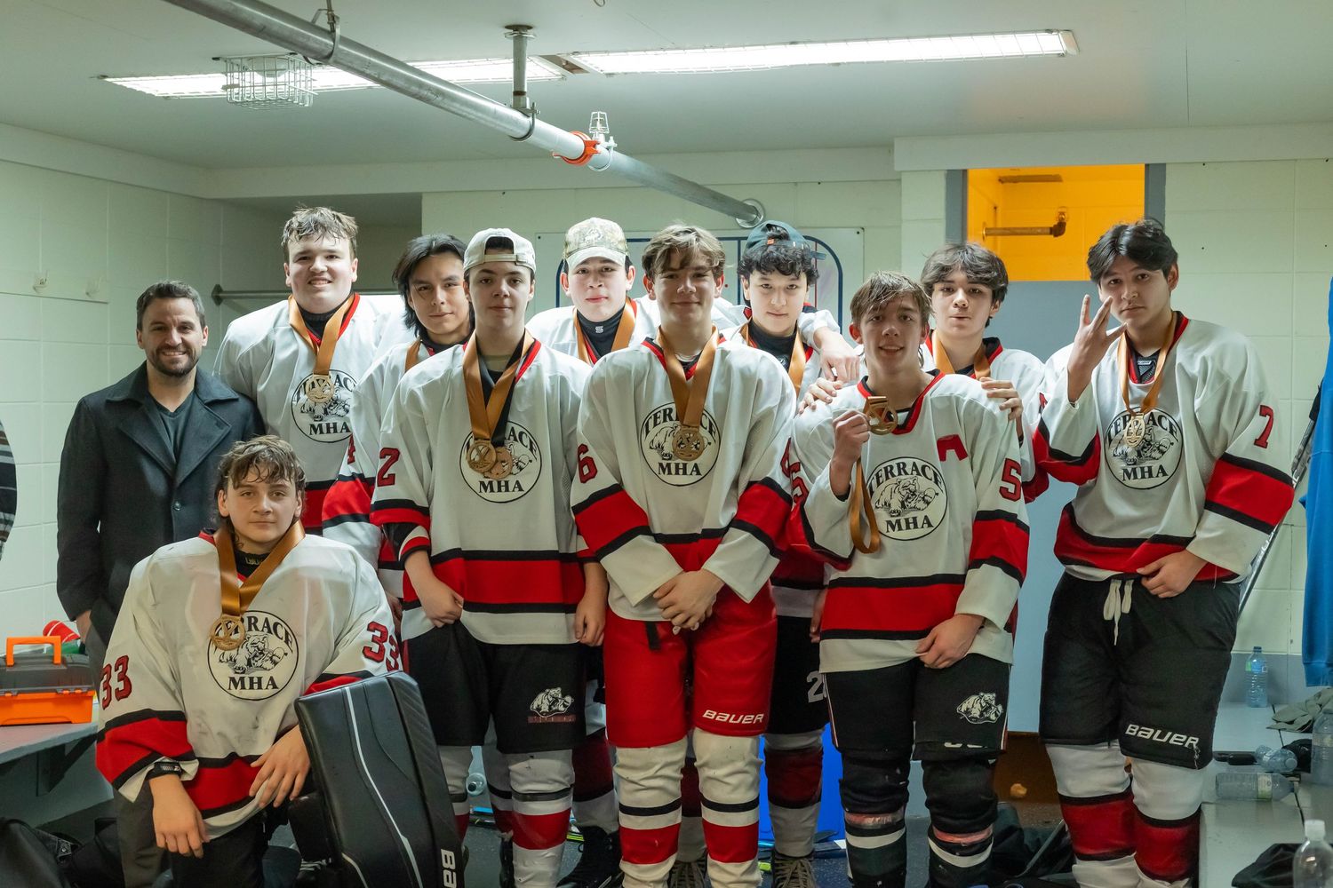 Hockey team in white and red jerseys poses with medals in locker room.