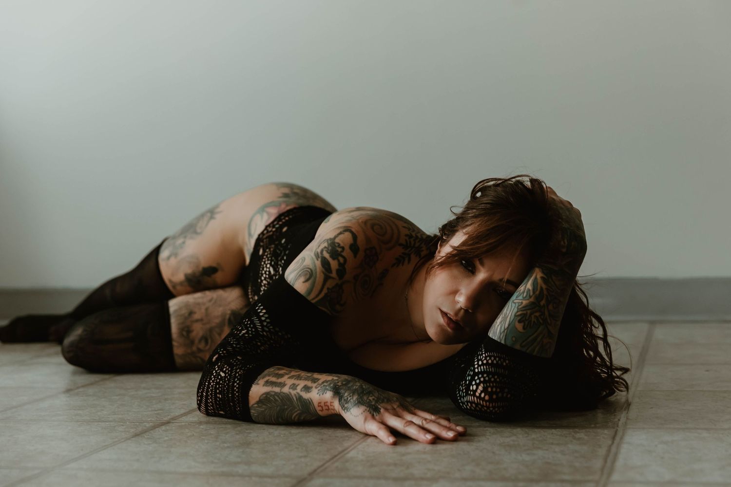 Dramatic portrait of person in dark outfit laying on floor with artistic lighting.