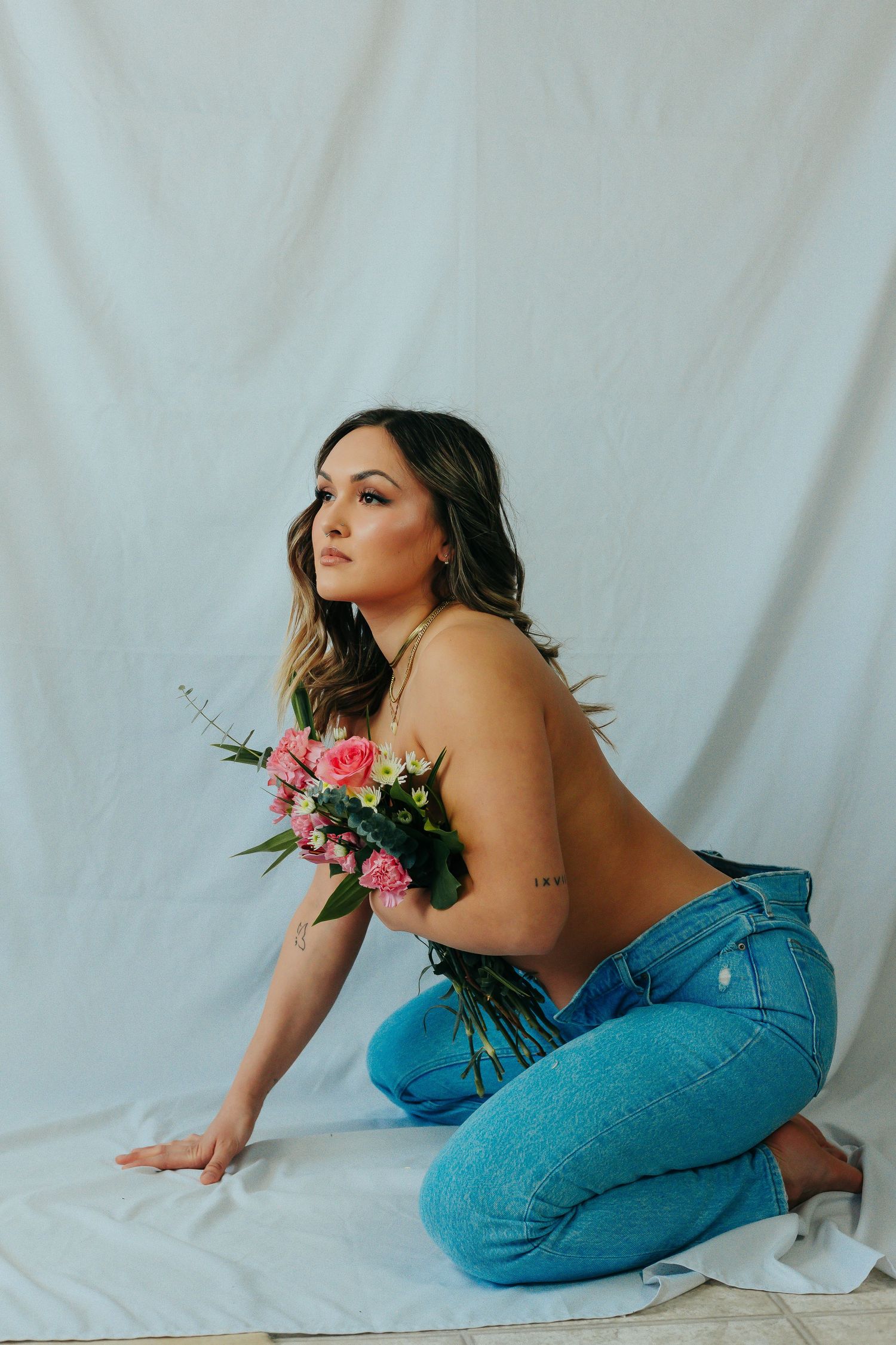 Artistic portrait against white backdrop featuring denim and fresh floral bouquet.