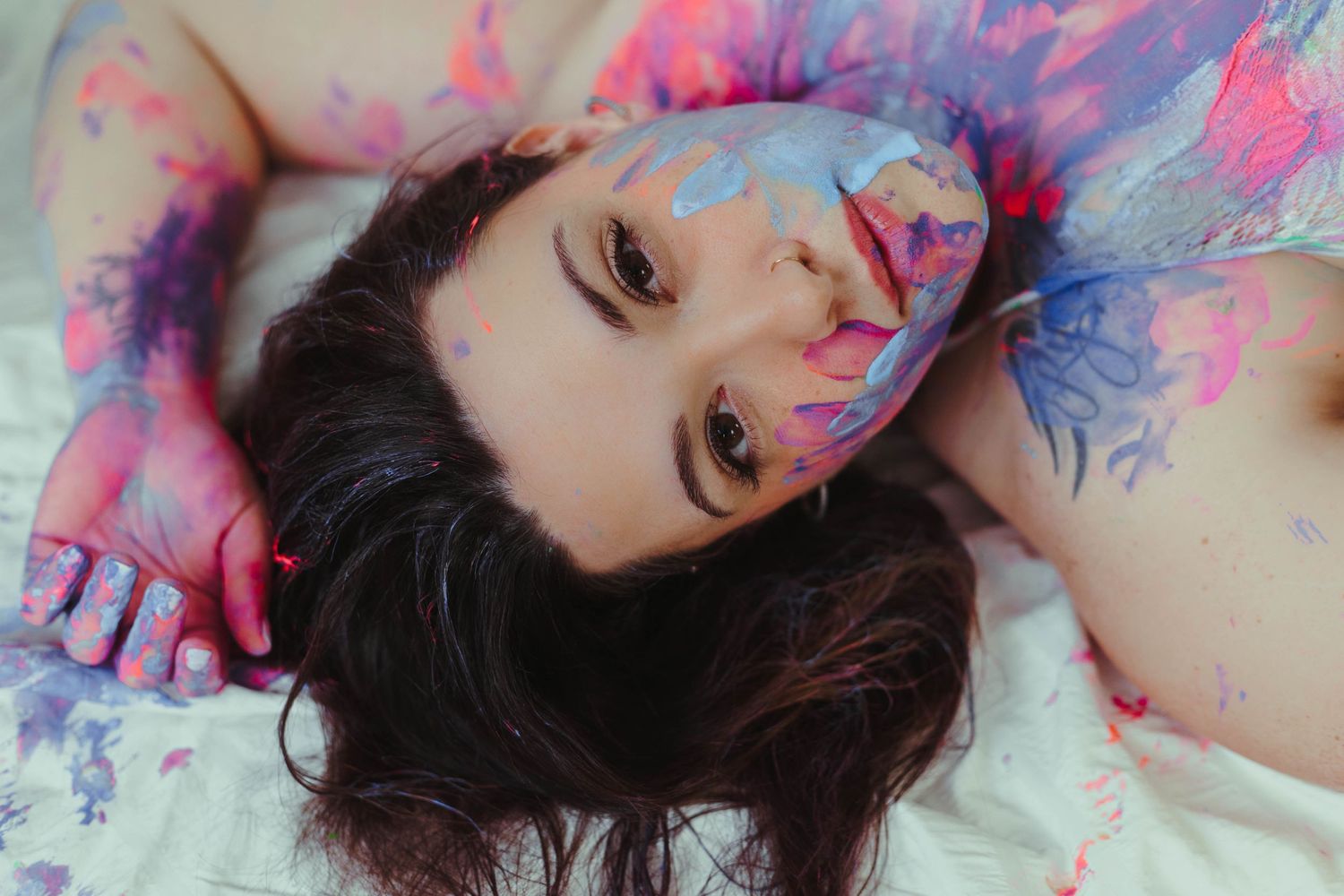 Creative portrait with splashes of pink and blue paint creating an artistic ethereal effect.