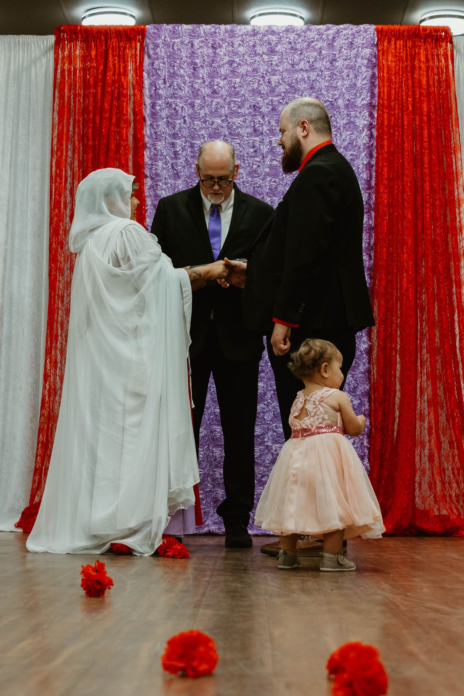 Wedding ceremony in progress with red and purple decor and flower petals on dance floor.