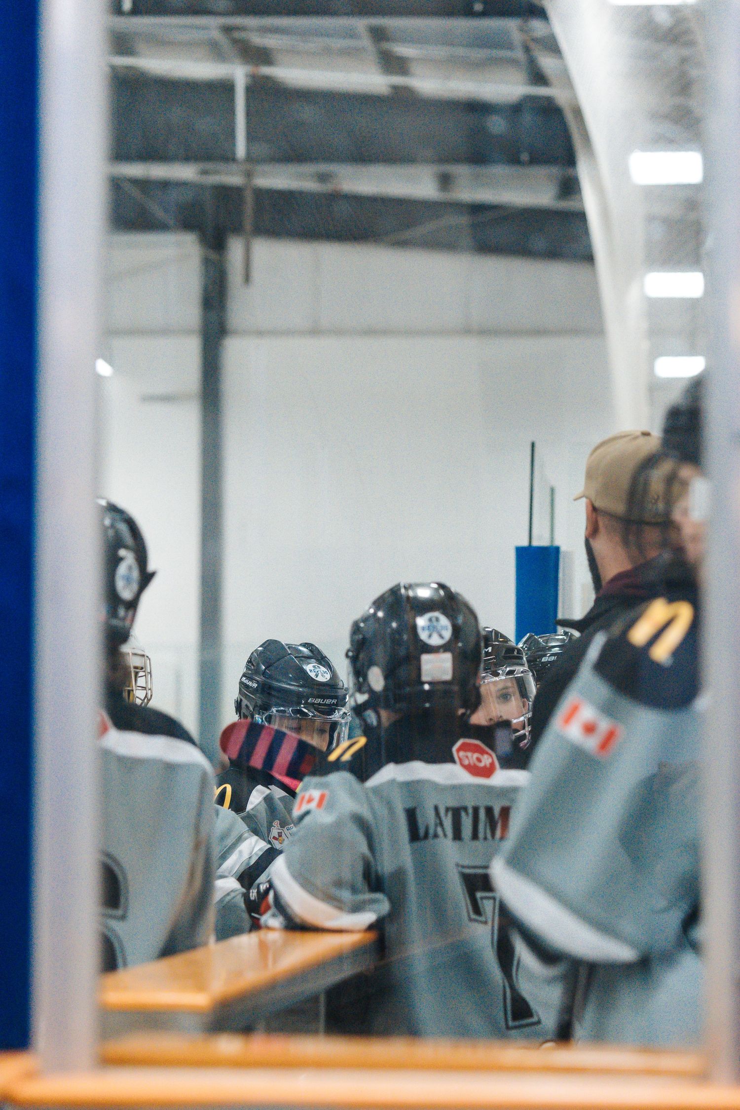 Hockey players in black helmets gather near the bench during a game viewed through glass.
