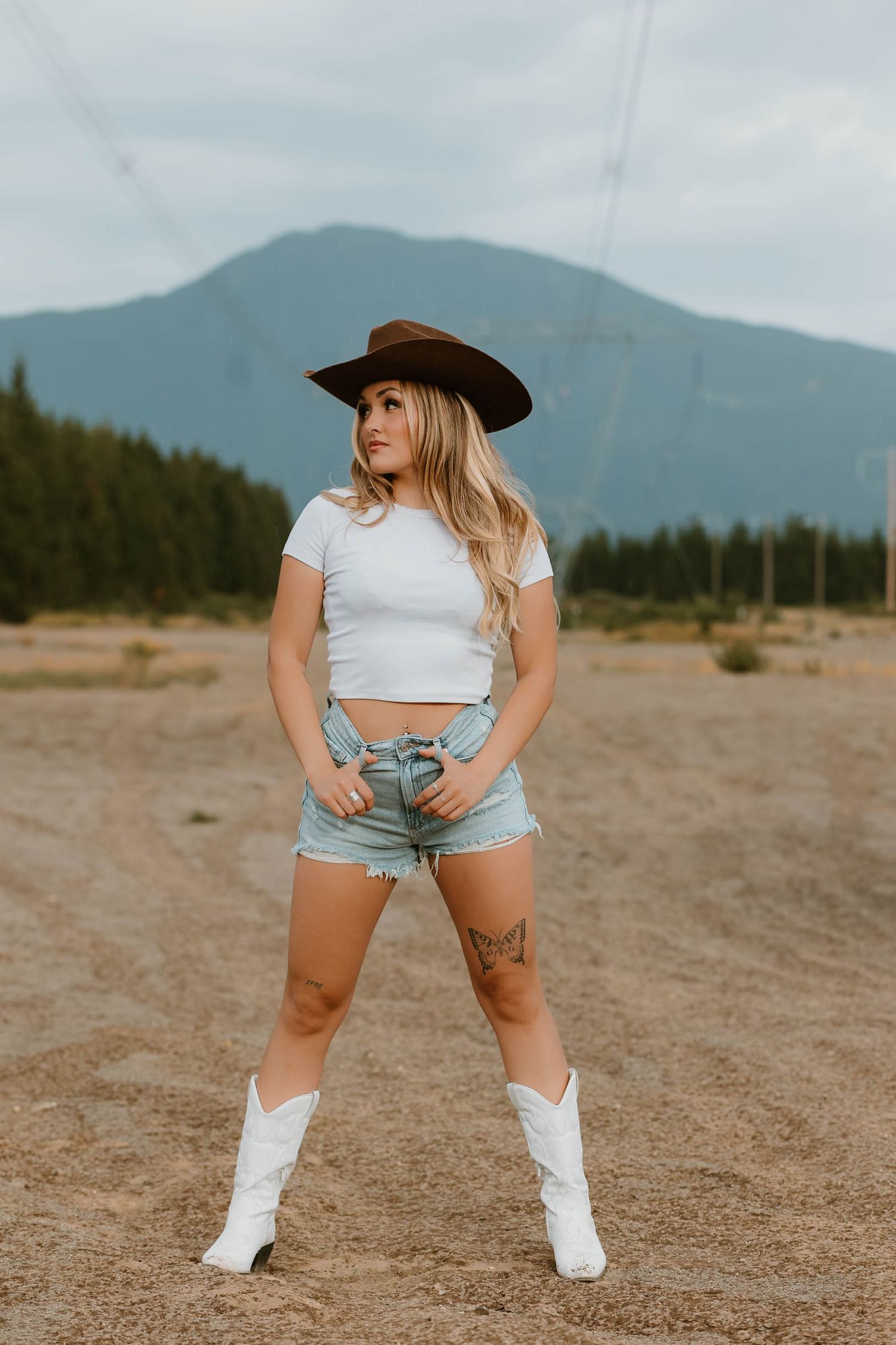 Western-style outfit with cowboy hat, crop top and boots against mountain backdrop.