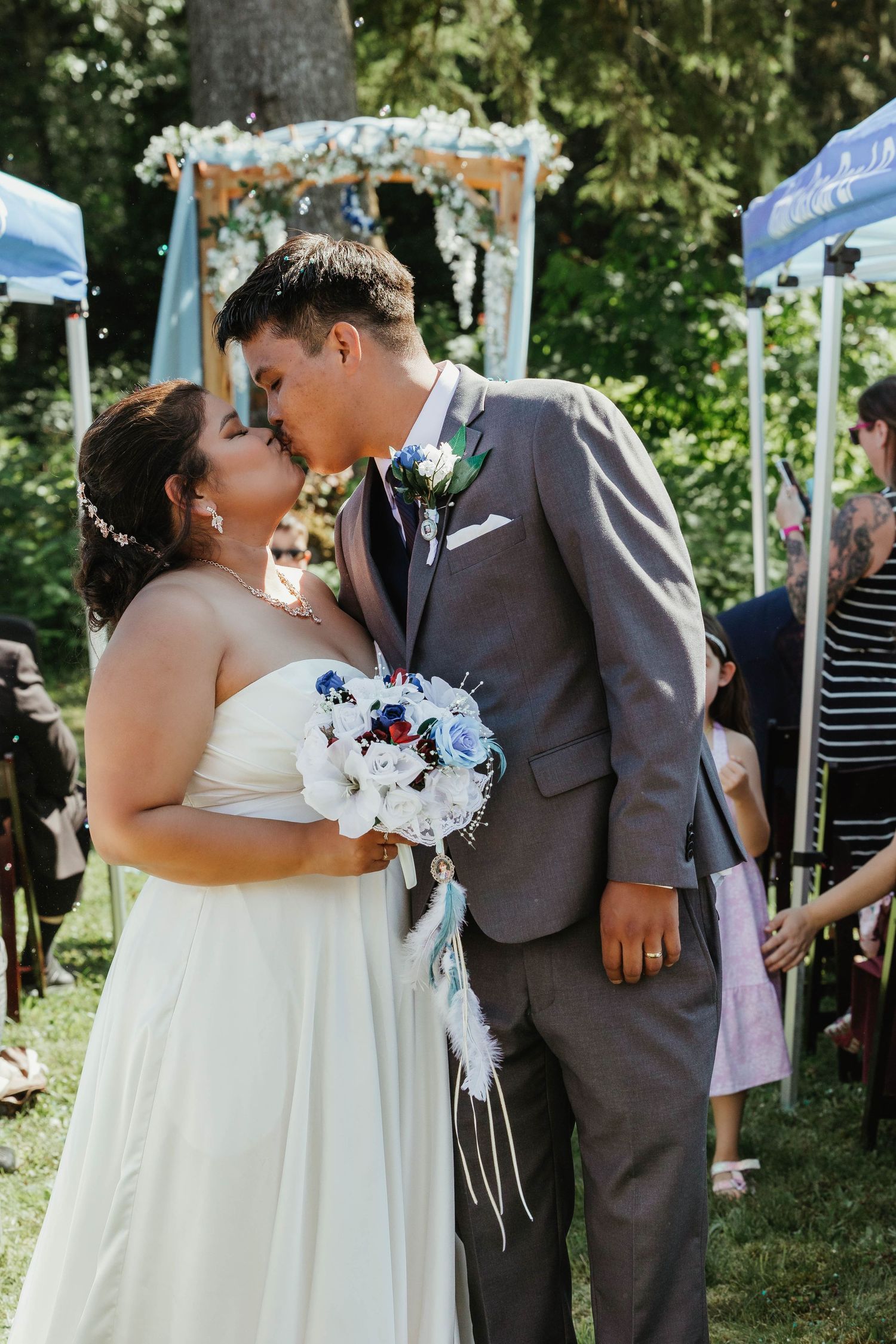 Romantic moment between newlyweds under a floral arch with blue and white bouquet.