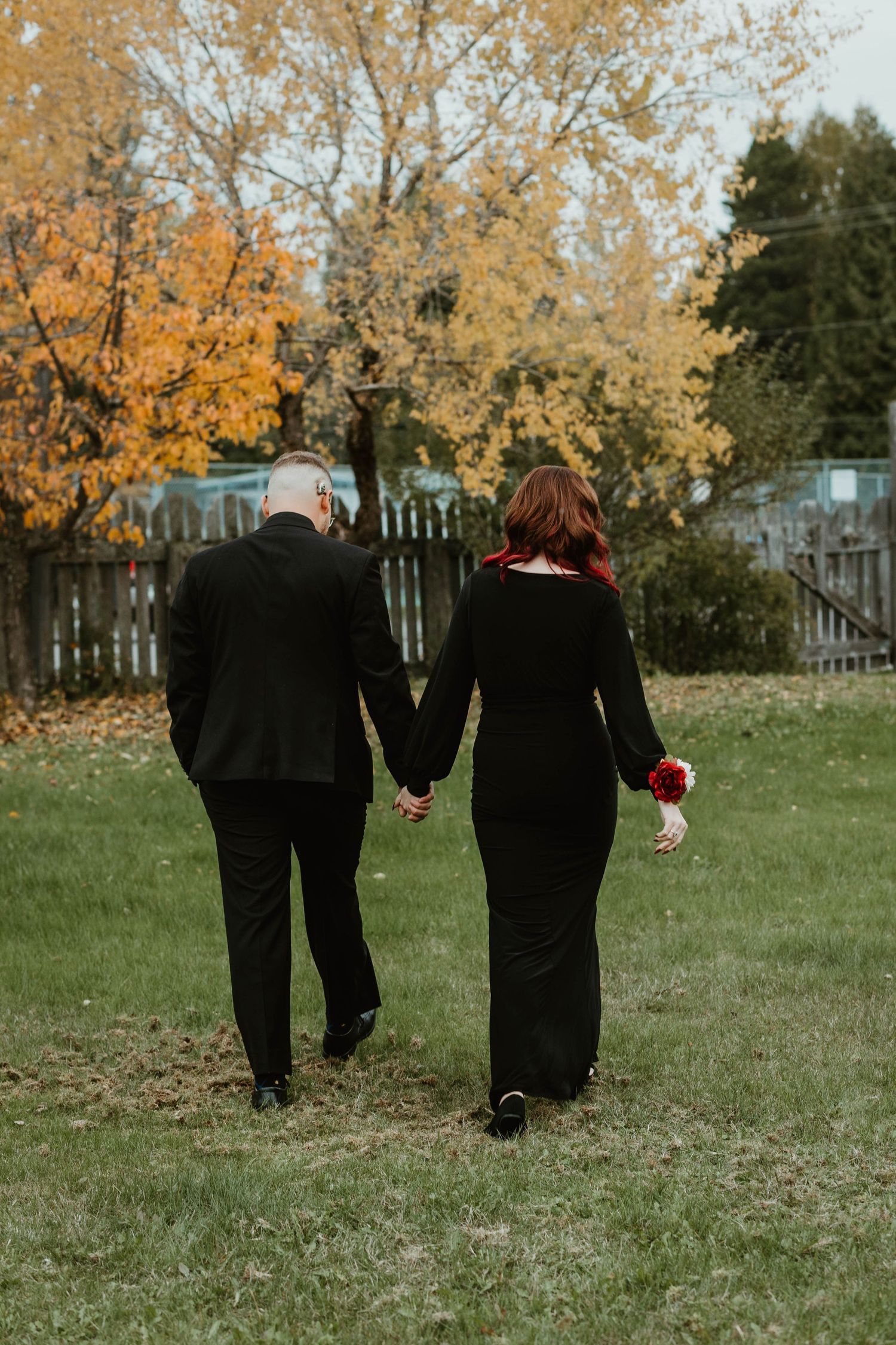A couple walks hand in hand through a fall garden with golden leaves in the background.