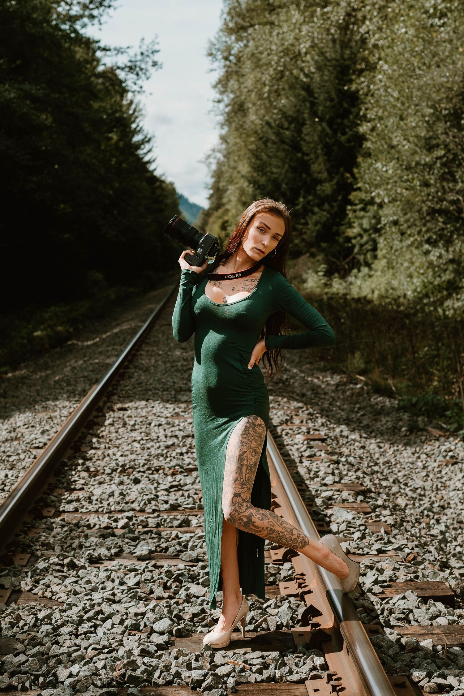 Figure in emerald green dress poses elegantly on train tracks through a forest.