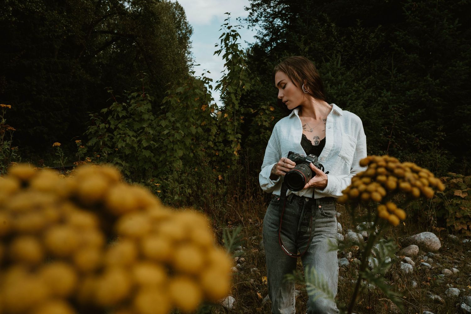 Photographer with camera stands amid blooming yellow flowers in natural outdoor setting.