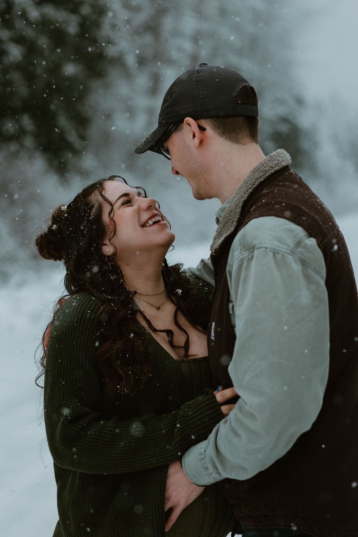 A joyful winter moment between a couple laughing in falling snow.